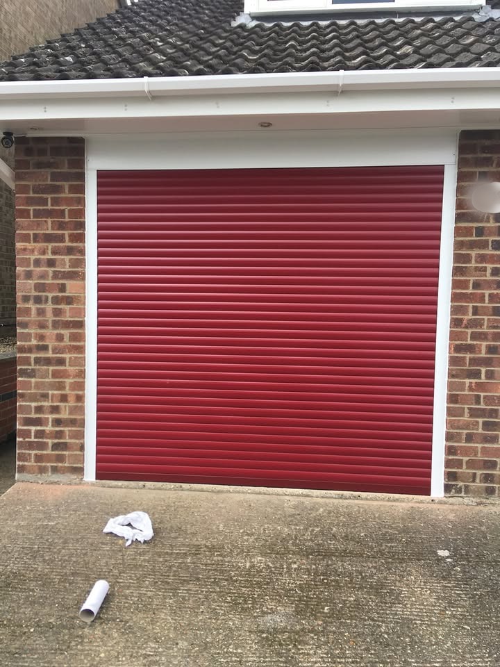 Red roller garage door fitted with white frame on a brick garage