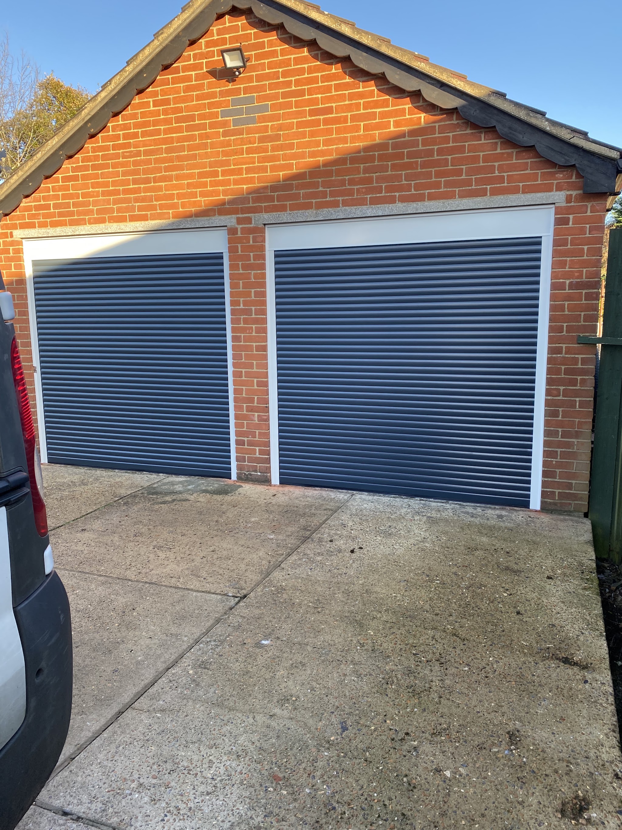 Two blue roller garage doors fitted on a red-brick double garage