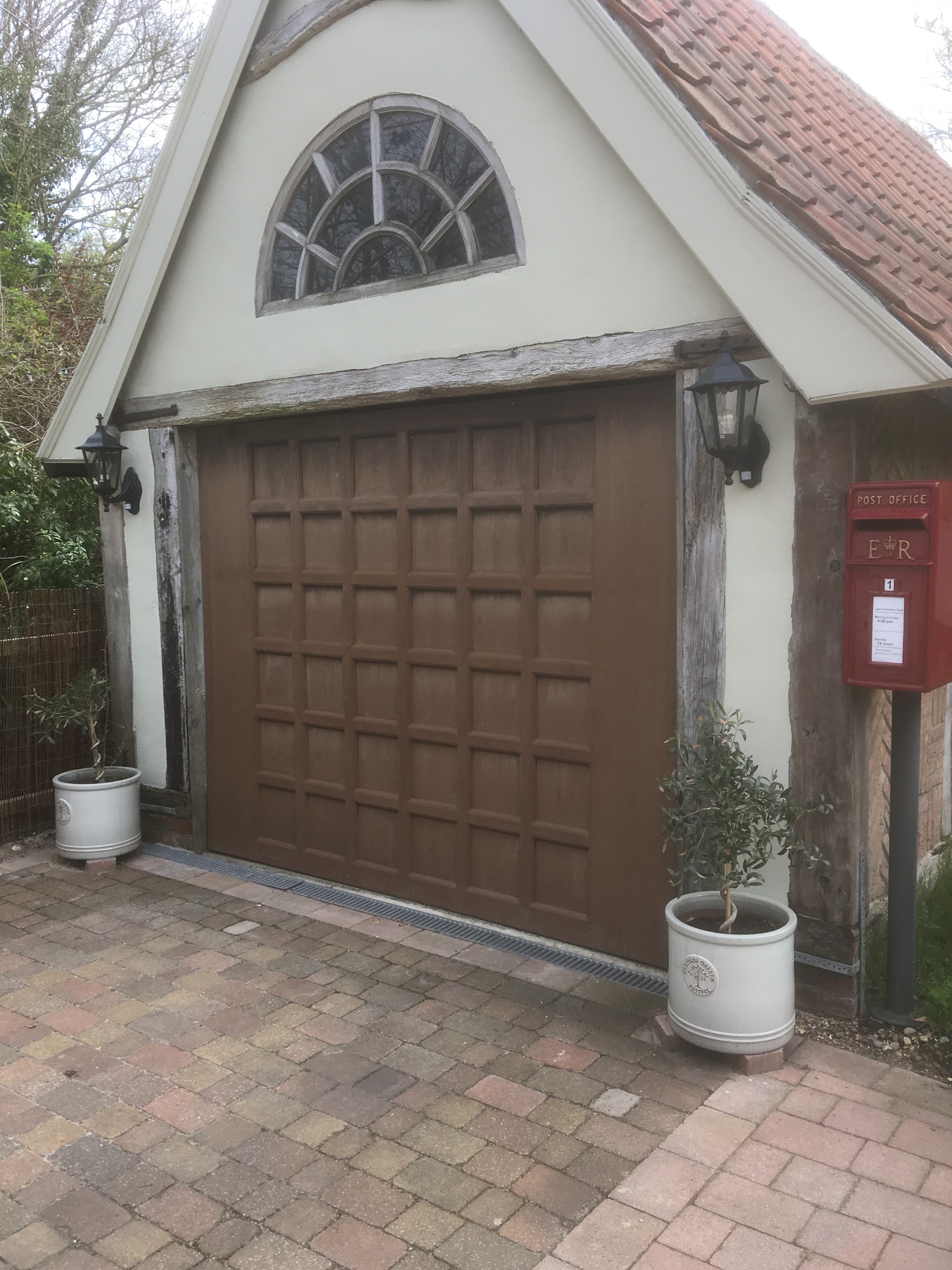 Oak-finish panelled garage door on a white-rendered cottage garage with lanterns either side