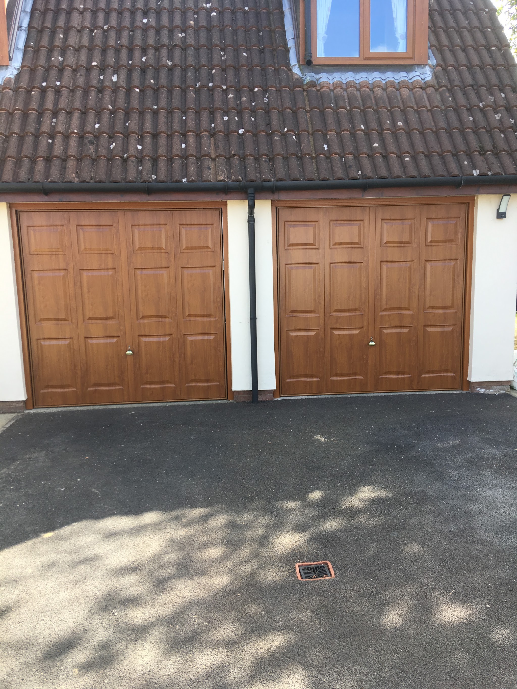 A pair of golden-oak panelled garage doors fitted on a double garage with a fresh tarmac drive