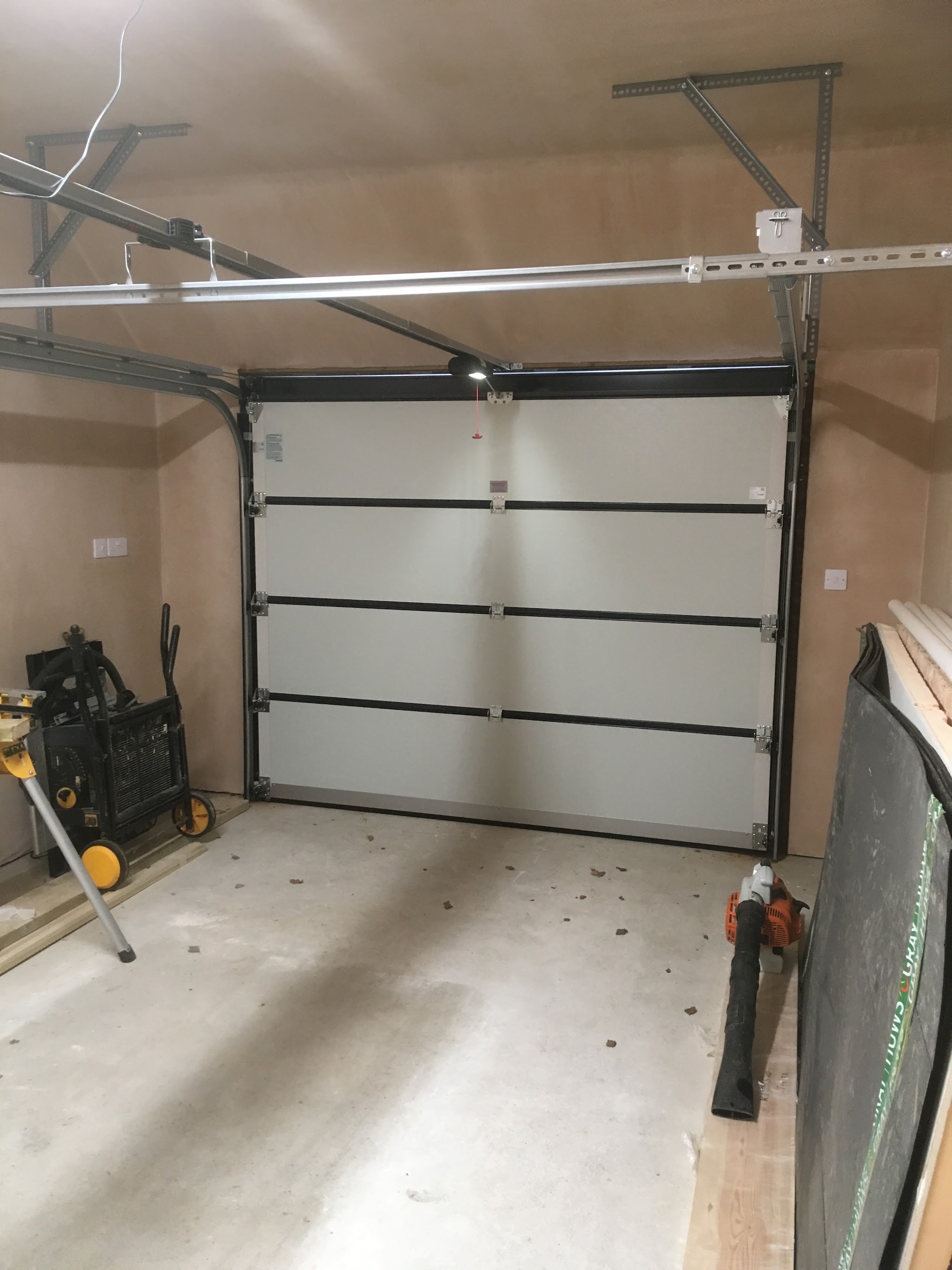 Inside a plasterboarded garage looking at a white sectional door with an electric operator rail above